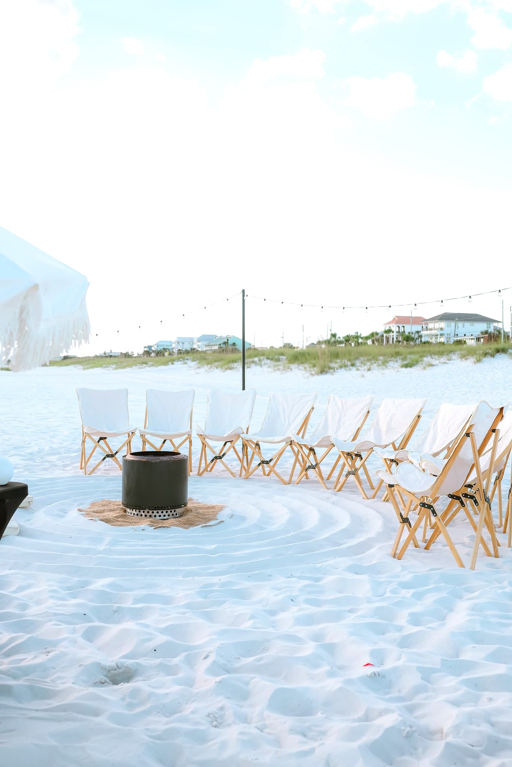 A row of styled white sling chairs with a fringed umbrella