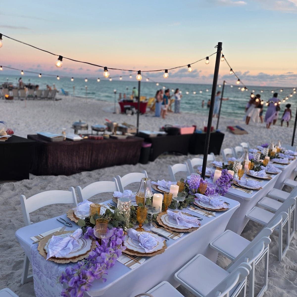 The full Seaside Supper dinner table under string lights at sunset over the Gulf